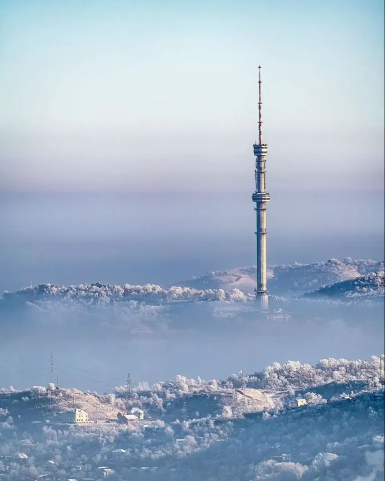 Almaty television tower above a snow-covered hillside and city haze