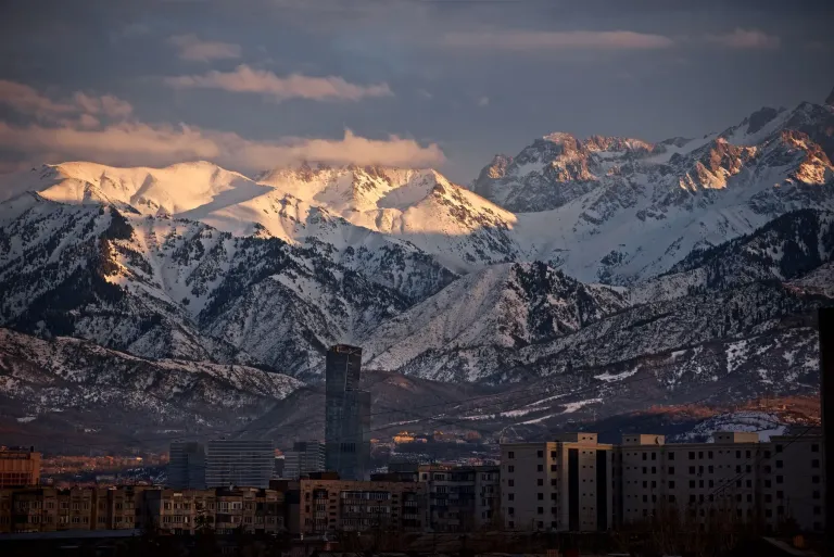 Almaty buildings below snow-covered mountains at dawn