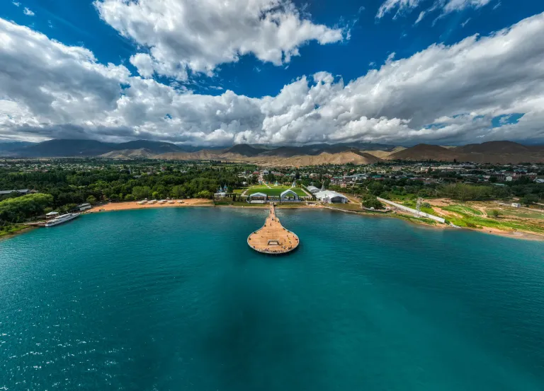 Aerial view of a curved beach and pier on turquoise Issyk-Kul