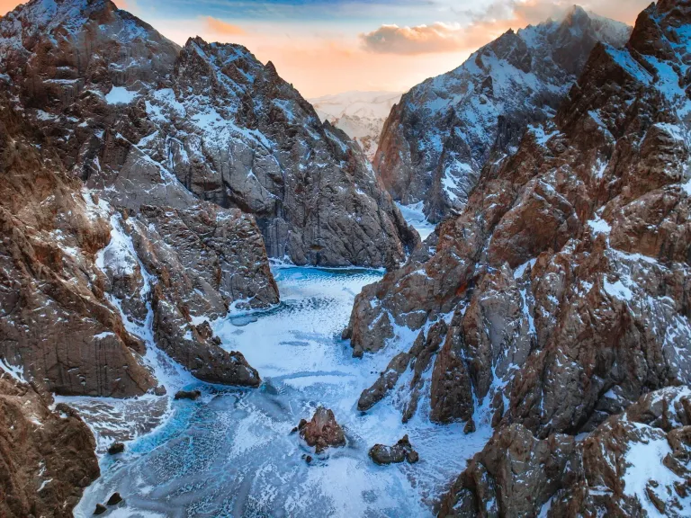 Frozen river winding between snow-dusted canyon walls at sunset