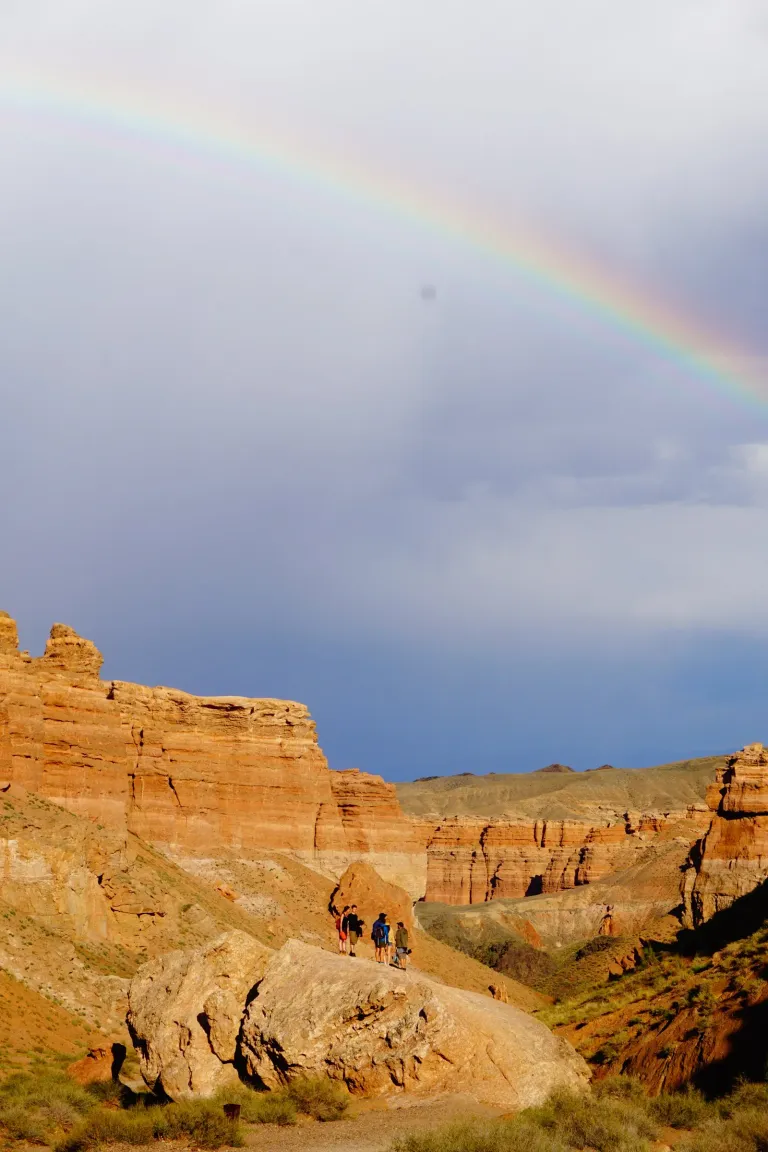 Hikers beneath a rainbow over the red cliffs of Charyn Canyon, Kazakhstan