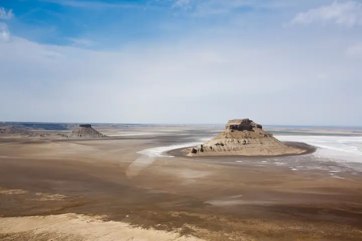 Isolated rock outcrop surrounded by the pale flats of Karyn-Zharyk